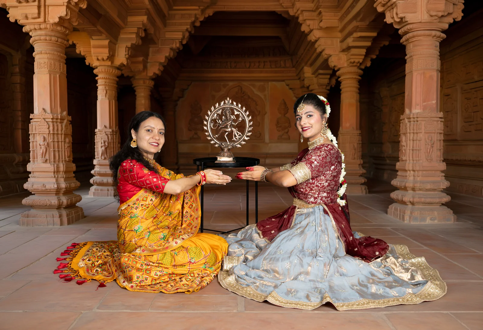 Smt. Hiral Joshi and Jia seated in a temple, hands joined over a Nataraja idol in a gesture of blessing